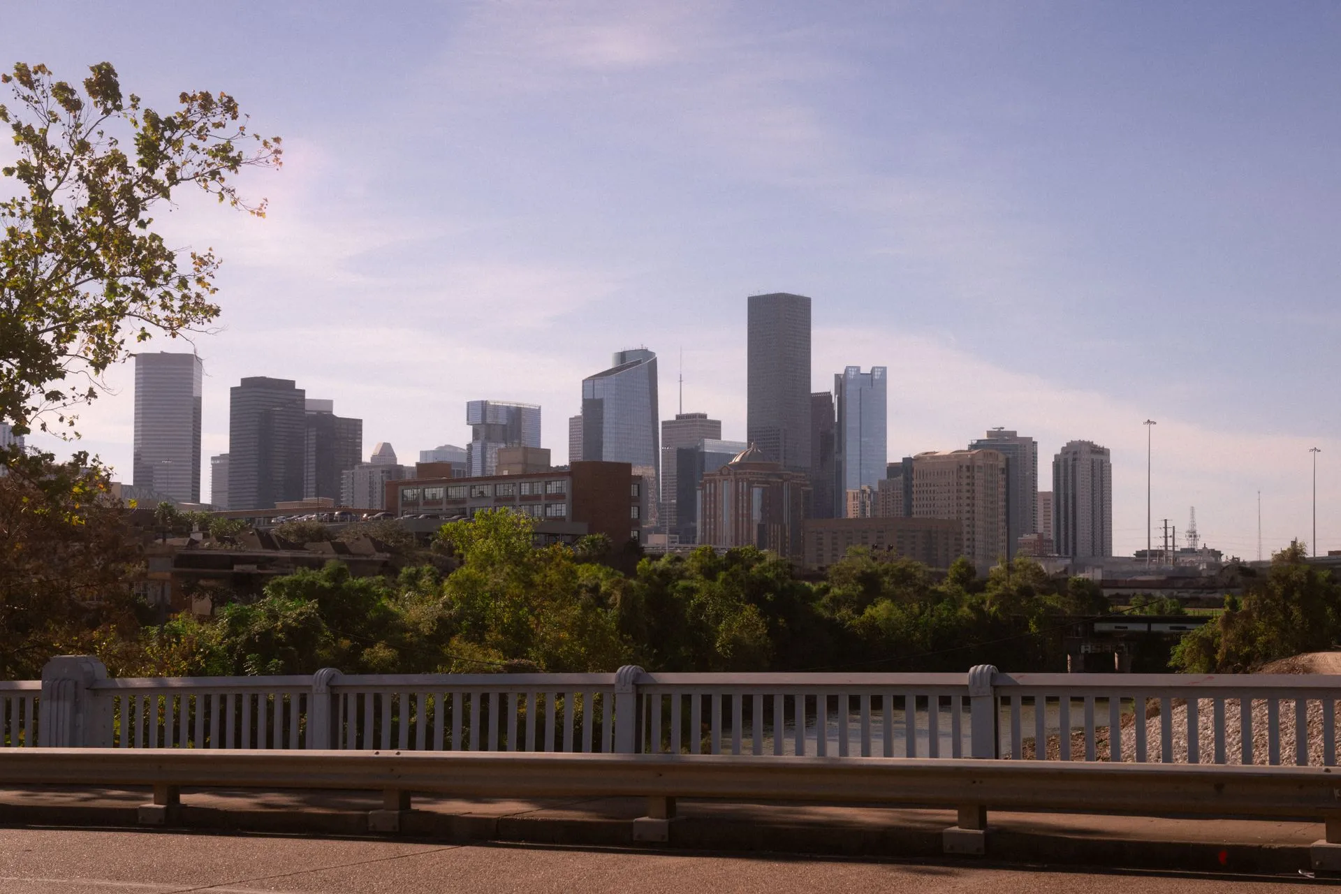 Downtown Houston skyline viewed across a tree-lined bridge